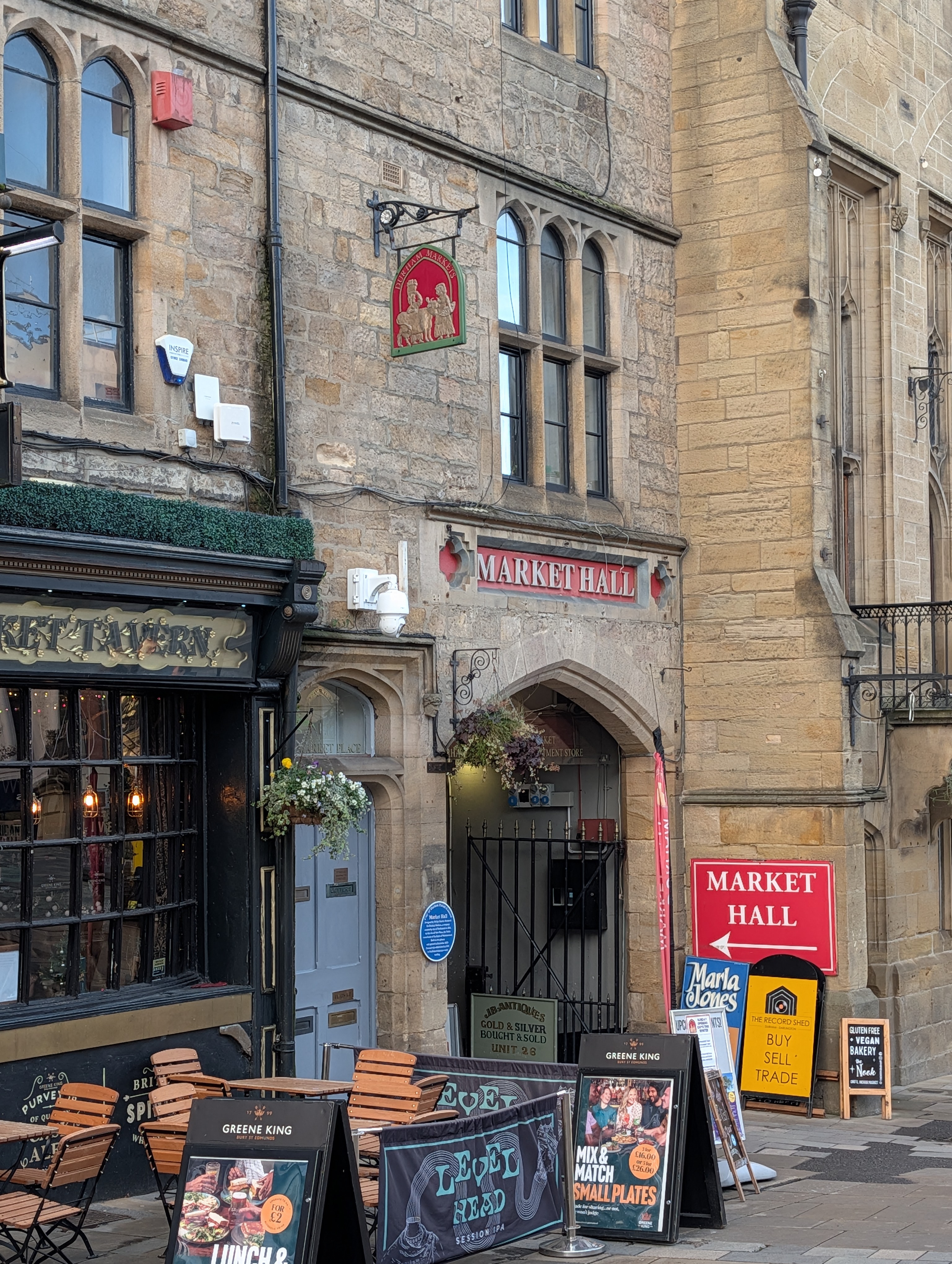 The historic stone exterior and arched entrance of Durham Market Hall, featuring traditional red signage and pavement boards alongside the Market Tavern pub
