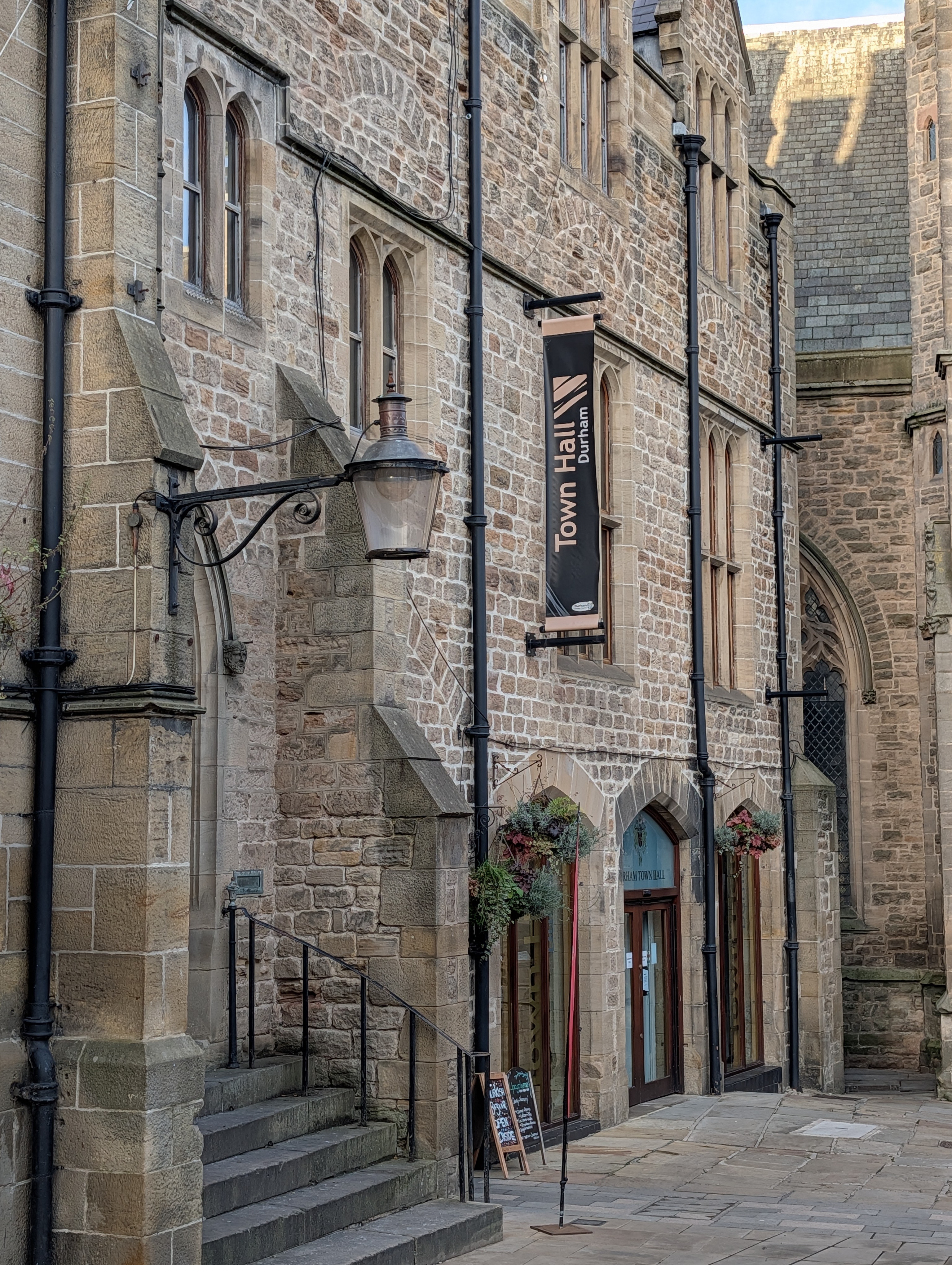 The exterior stone facade, gothic windows, and arched entrance of the historic Durham Town Hall, featuring traditional lanterns and hanging plants