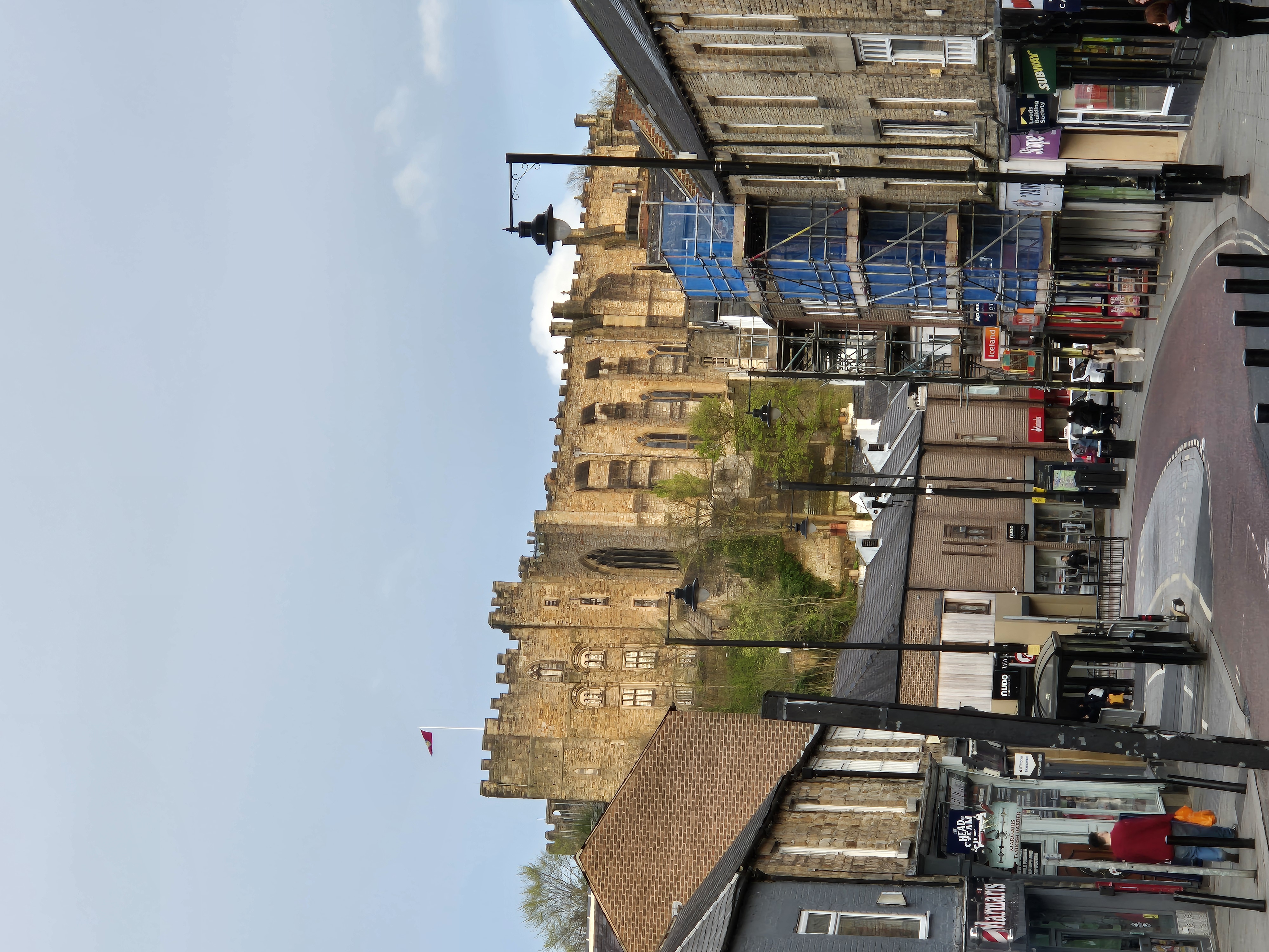 View of the historic stone structure of Durham City Castle towering over the cobbled streets and modern shop fronts of the city centre below